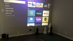 A room with a large screen displaying a streaming service interface, a ceiling fan, and a chessboard on the floor.