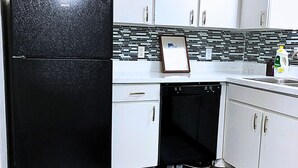 A kitchen with white cabinets, a black refrigerator, a dishwasher, and a tiled backsplash.