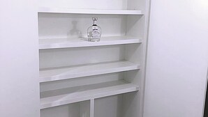 A white closet with multiple shelves and a hanging rod, a bottle of hand sanitizer, and a toilet with a marble design.