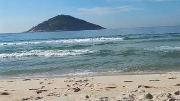 Uma praia com pegadas que levam à água, céu claro e uma ilha ao longe.