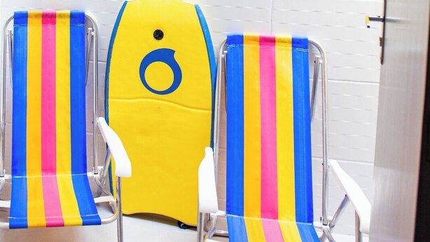 Two striped beach chairs in a bathroom with a yellow wall and white tiled floor.