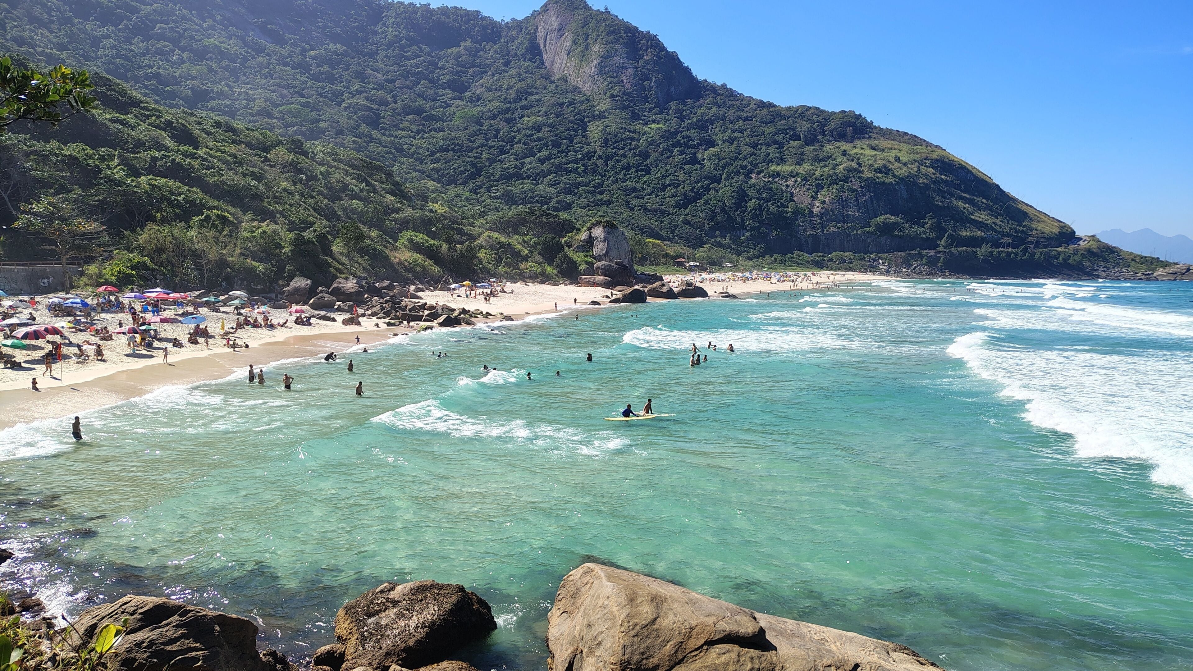 Une plage aux eaux turquoise et limpides, bordée de formations rocheuses et dominée par un paysage montagneux.