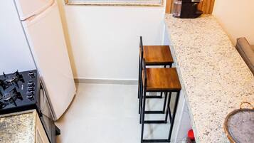 Uma cozinha compacta com geladeira, fogão, dois bancos e uma janela.