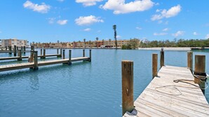 A wooden pier extending into calm water with a clear sky and distant buildings. - Turtle Nest (Sarasota)