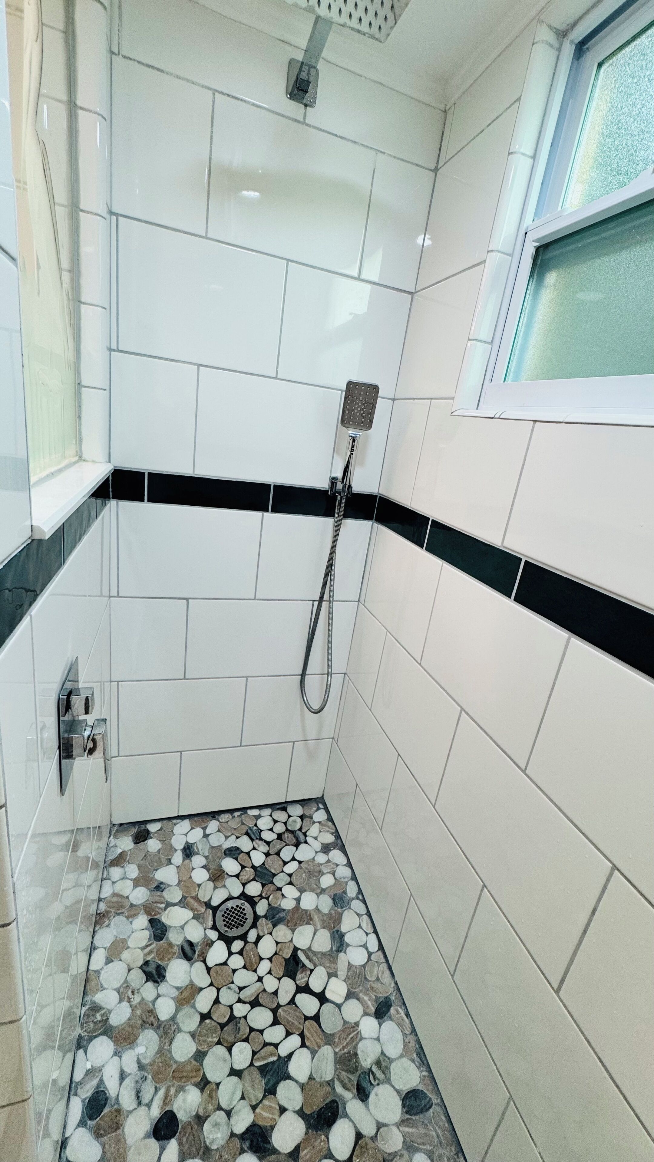 Un pequeño espacio de ducha con azulejos, piso de guijarros y una ventana.