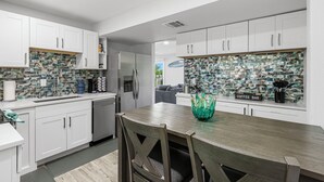 A modern kitchen with white cabinets, a tiled backsplash, and a coffee bar area. - Turtle Nest (Sarasota)