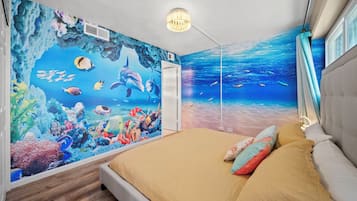 Een slaapkamer met een muurschildering van een onderwaterlandschap, een bed met beige beddengoed en een moderne plafondlamp.