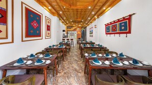 Ein Restaurant mit Holzbalkendecke, Marmorboden und Tischen, die mit blauen Servietten und weißen Tellern gedeckt sind.