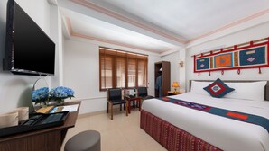 Ein Hotelzimmer mit einem Bett, einem Schreibtisch mit Computer, einem Fernseher und einem Fenster mit Jalousien.