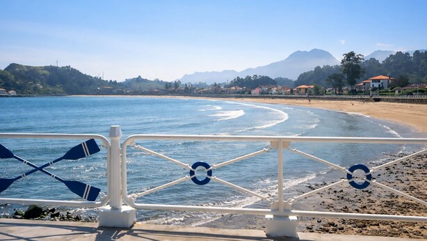 A beach view from a boat with a railing, a clear sky, and distant mountains. - Ribadesella House with Garden 2 km from Beach – Saelia (Ribadesella)