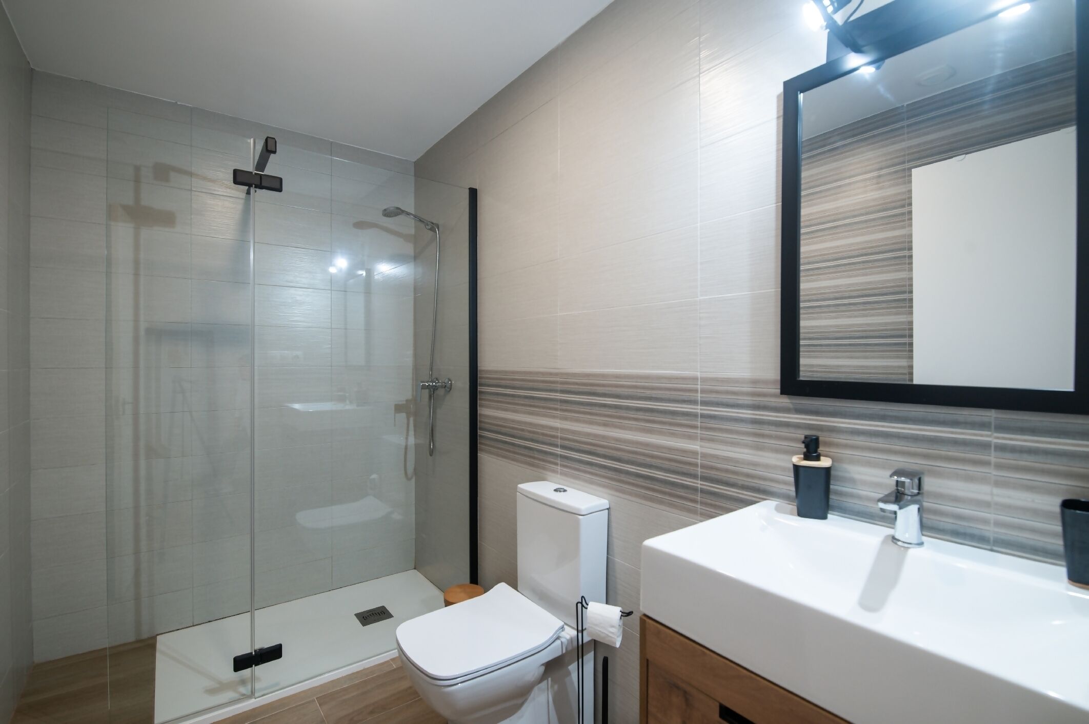 A modern bathroom with a glass shower enclosure, a white toilet, a sink with a mirror, and a towel rack.