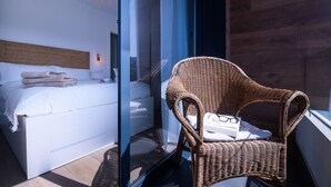 A bedroom with a bed, a wicker chair, and a glass partition. - Ribadesella House with Garden 2 km from Beach – Saelia (Ribadesella)