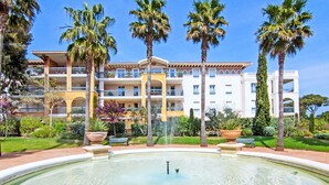 A hotel with a large fountain in the courtyard, surrounded by palm trees and a well-maintained garden. - Le Grand Parc by Interhome (Saint Aygulf)