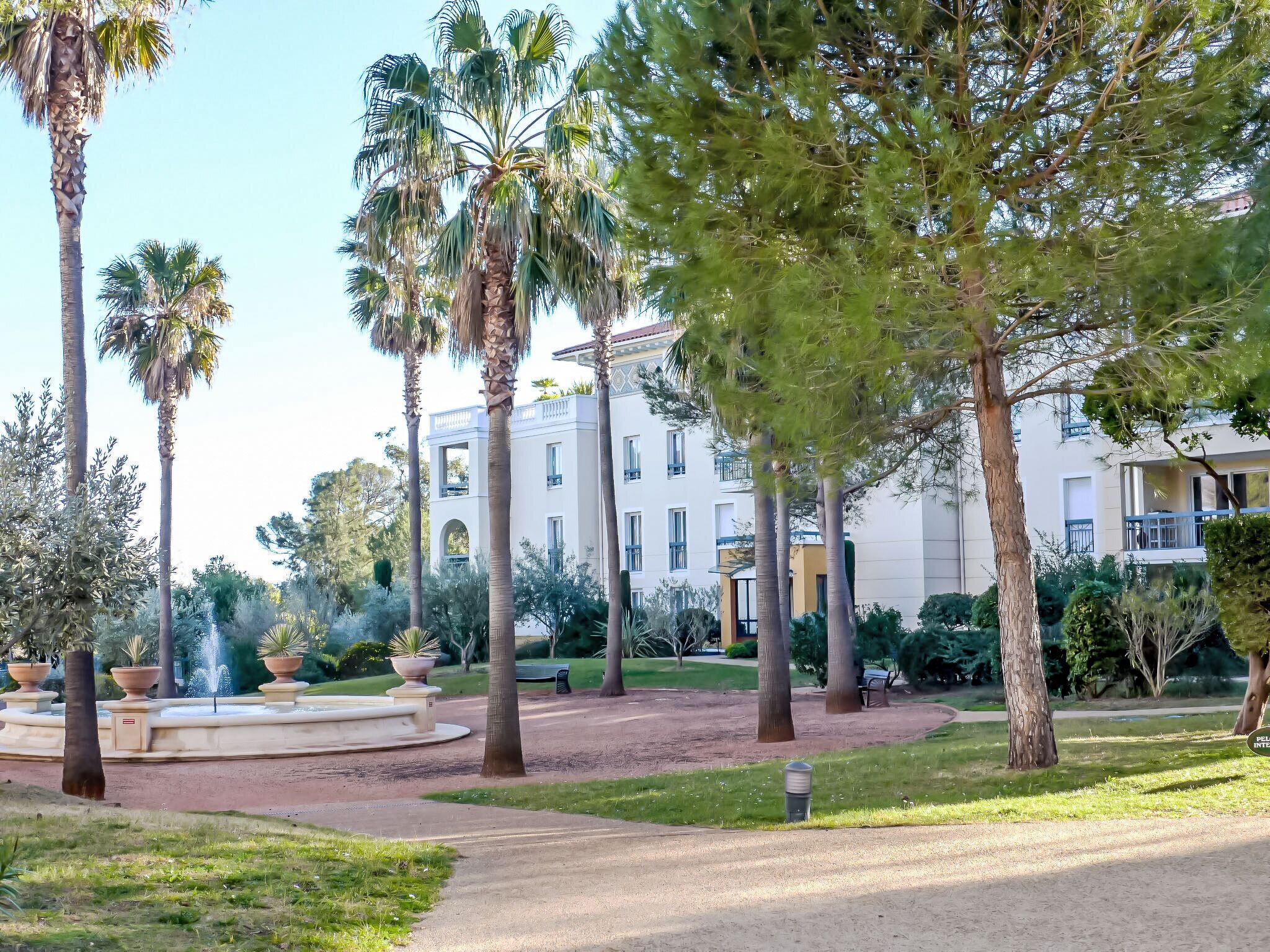 Jardim ajardinado com palmeiras, uma fonte e um edifício com várias varandas.