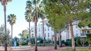 A landscaped garden with palm trees, a fountain, and a building with multiple balconies. - Le Grand Parc by Interhome (Saint Aygulf)