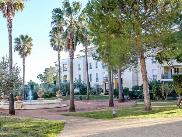A landscaped garden with palm trees, a fountain, and a building with multiple balconies.