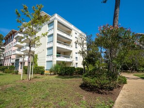 Um edifício com várias andares e varandas, rodeado por vegetação e um céu limpo.