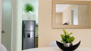 Uma área de refeições com uma mesa branca, tigela preta com plantas verdes e um espelho com moldura decorativa.