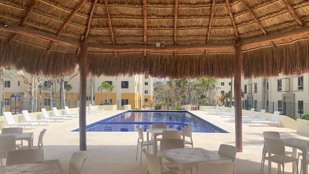 Uma área na piscina com telhado de palha, espreguiçadeiras e mesas.