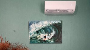 Quarto com cama, pintura de um surfista, vaso e mesa de cabeceira.