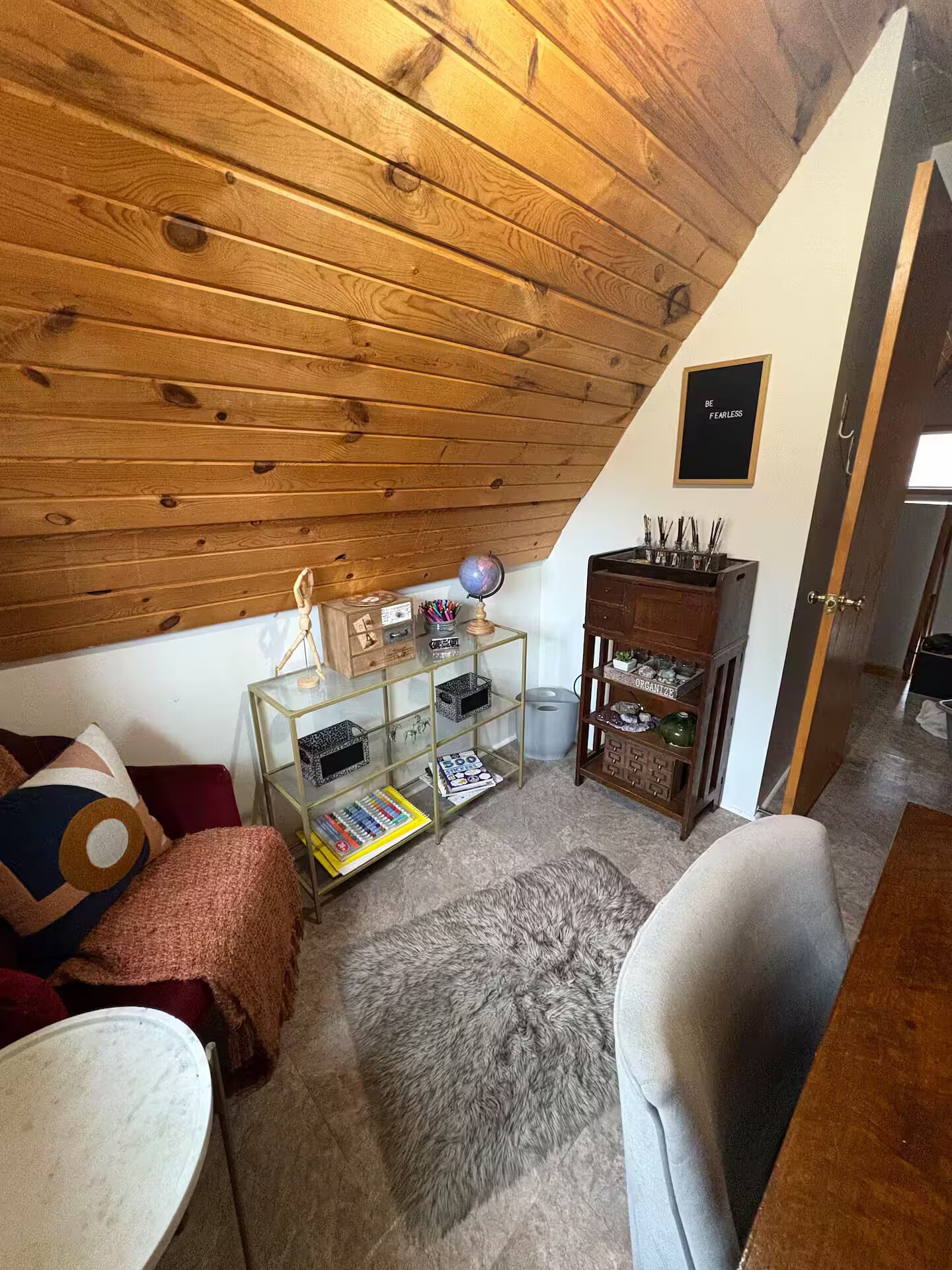 Acogedor dormitorio en ático con vigas de madera, una estantería, un globo terráqueo y un cartel motivacional.