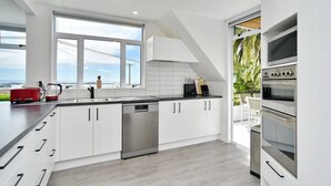 Una cocina moderna con armarios blancos, lavavajillas, una cafetera roja y un ventanal con vistas al exterior.