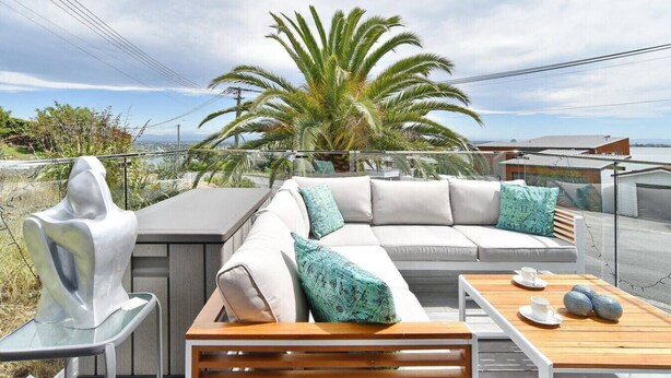 Una terraza en la azotea con un sofá blanco, cojines color aguamarina, una mesa de madera y una escultura de metal.