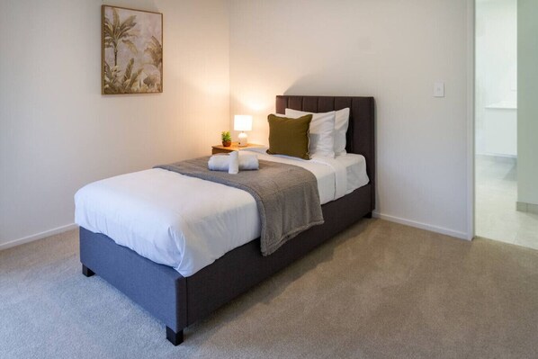 A neatly made bed with a grey headboard, a bedside lamp, and a small potted plant on the nightstand.