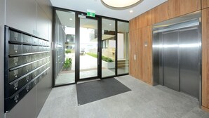 A modern elevator with a metallic finish, a glass door entrance with a green exit sign, and a series of mailboxes on the left. - Relax and Unwind Central City Hideaway with Carpark (Christchurch)