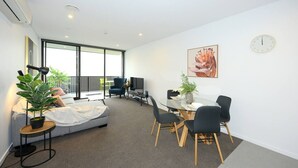 A modern living room with a sofa, a dining table with chairs, a large window, and a plant. - Relax and Unwind Central City Hideaway with Carpark (Christchurch)