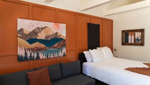 Een hotelkamer met een bed, een grijze bank, een schilderij van bergen en een raam met uitzicht.