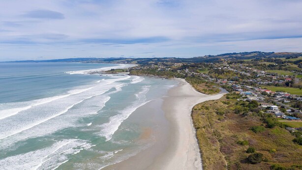 Une ville côtière dotée d’une plage de sable, offrant une vue dégagée sur l’océan, et comprenant un quartier résidentiel avec des maisons et de la verdure.