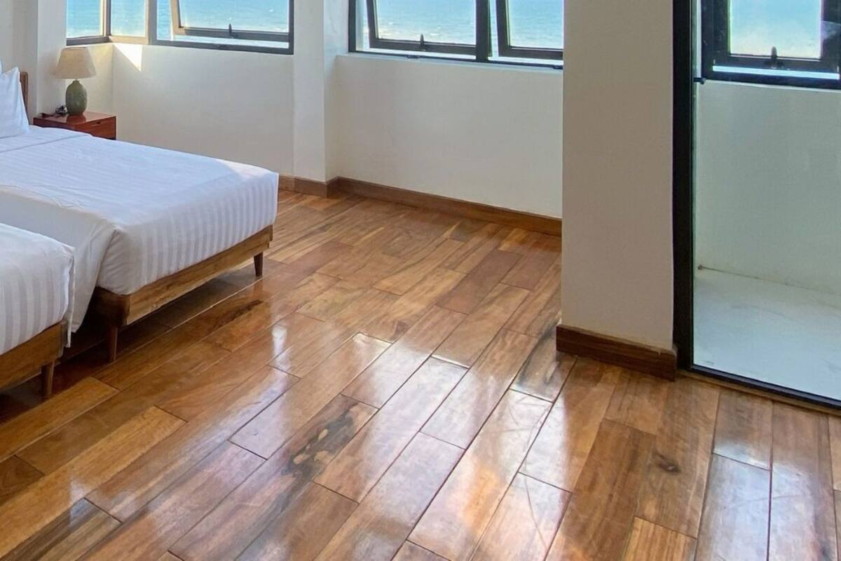 A hotel room with two beds, wooden flooring, large windows with ocean views, and a logo on the wall.