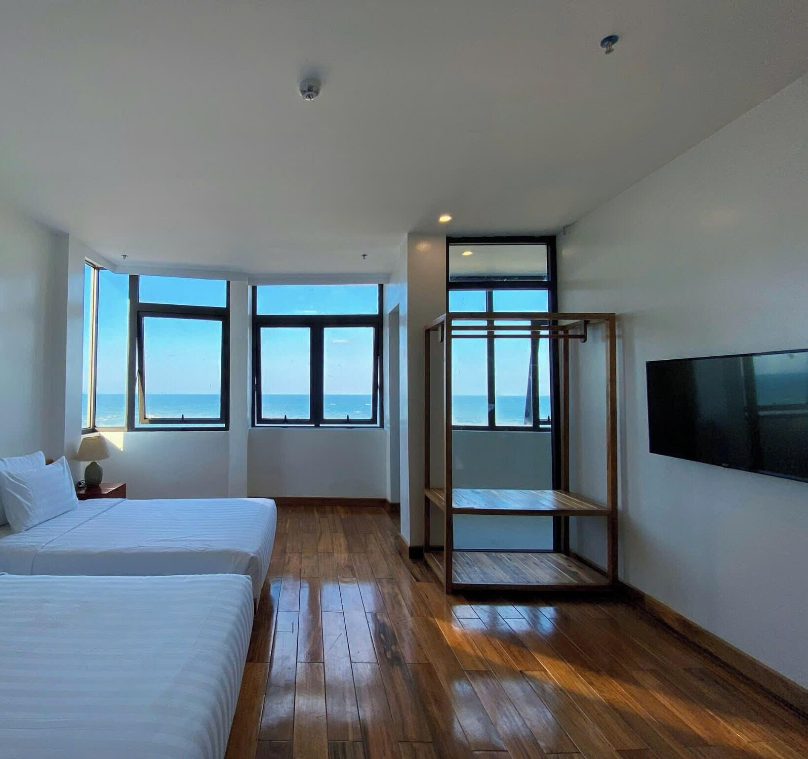 A modern hotel room with a large bed, a TV, and a view of the sea through large windows.