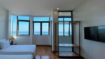 A modern hotel room with a large bed, a TV, and a view of the sea through large windows.