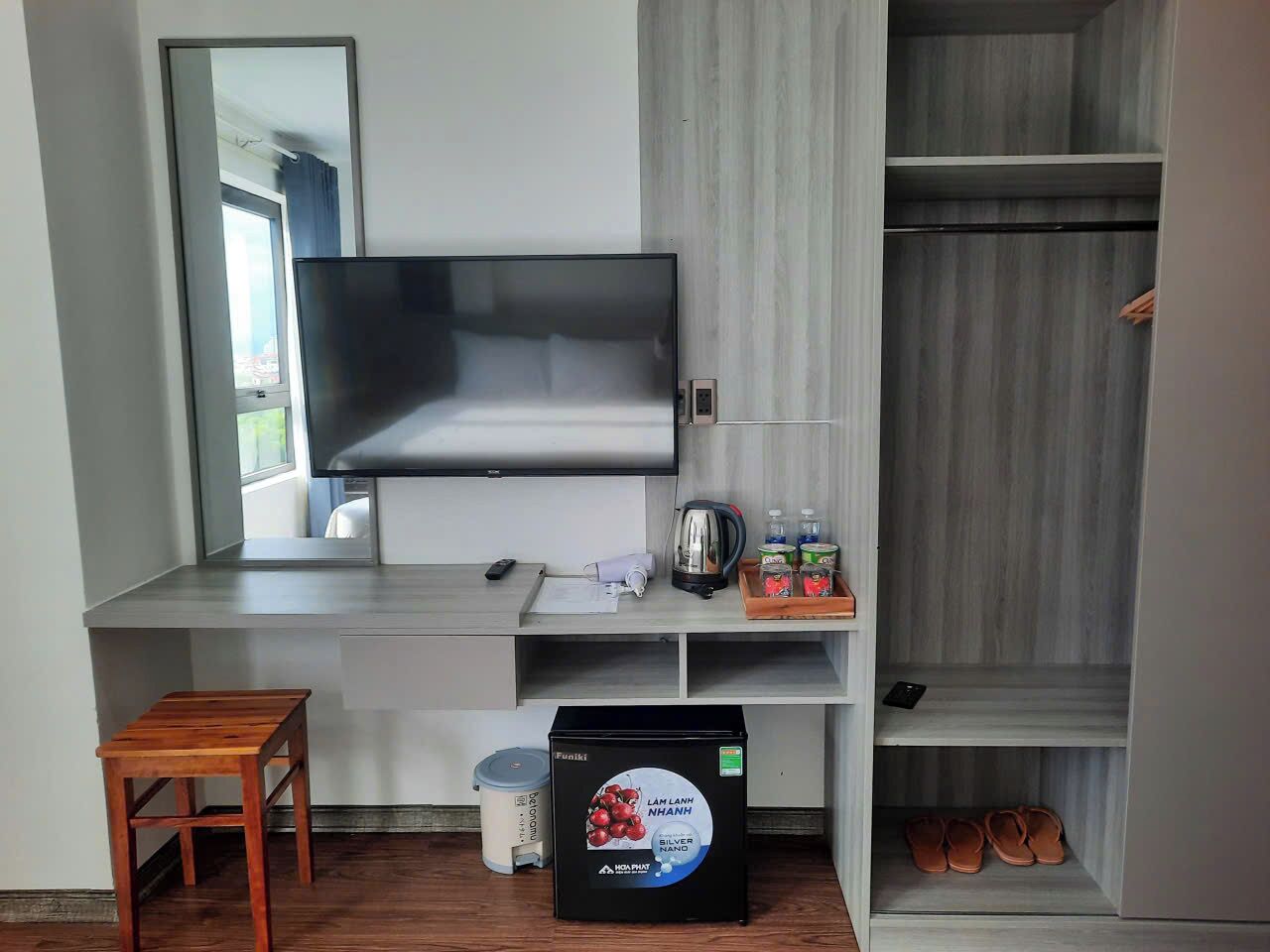 Quarto moderno com televisão de tela plana na parede, um pequeno banquinho de madeira, uma cafeteira e uma caixa de talheres.