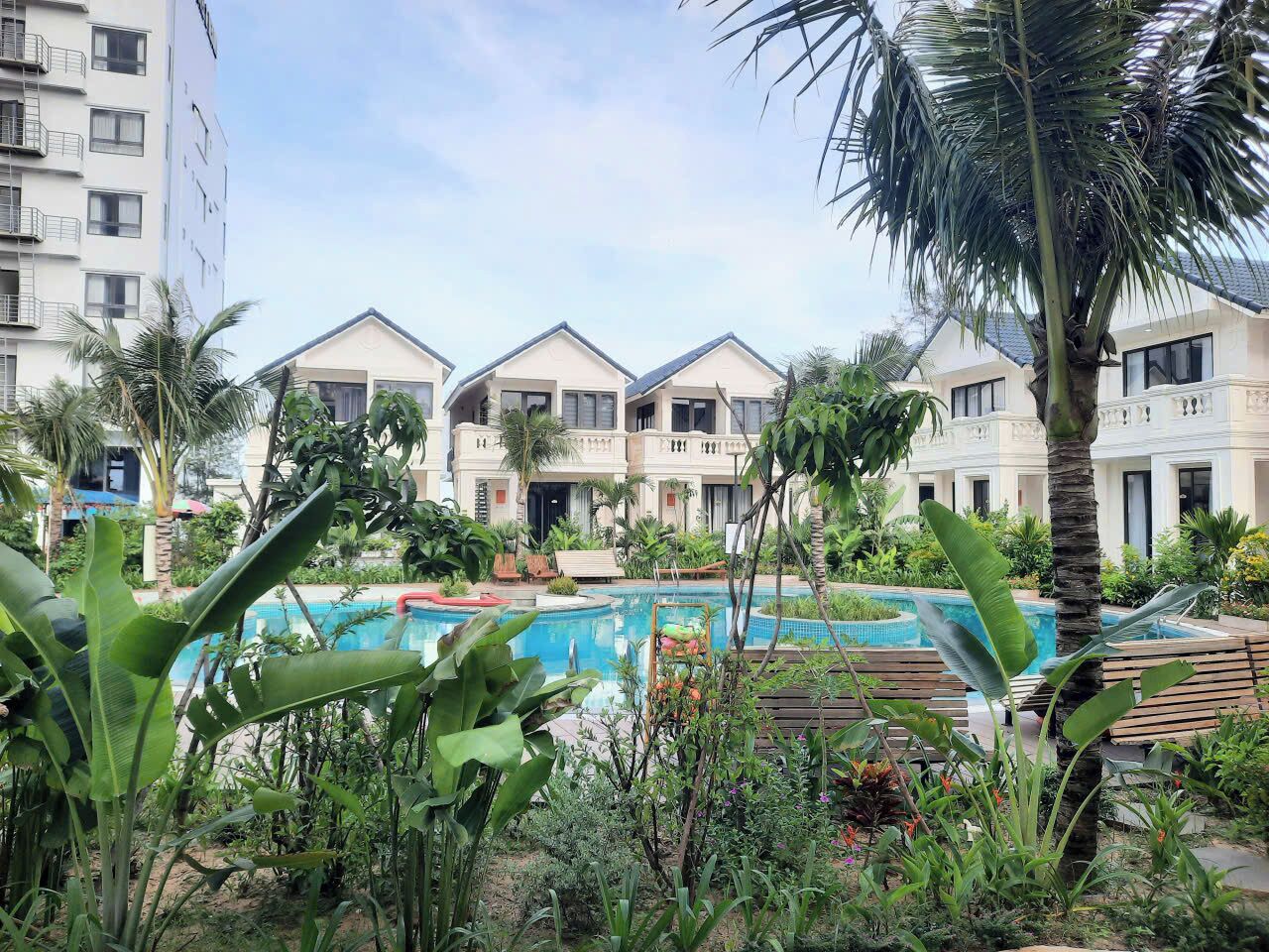 A hotel with multiple balconies, a swimming pool, and lush greenery.