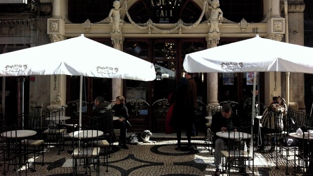 Ein Straßencafé mit aufwändiger Architektur, Sitzgelegenheiten im Freien und einem Hund.