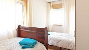 Ein Schlafzimmer mit zwei Einzelbetten, einem Holzkopfende und einem Fenster mit Vorhängen.