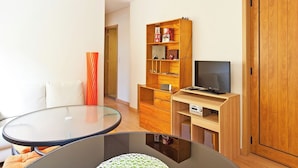 A modern room with a round glass table, a wooden bookshelf, a television, and a wardrobe.