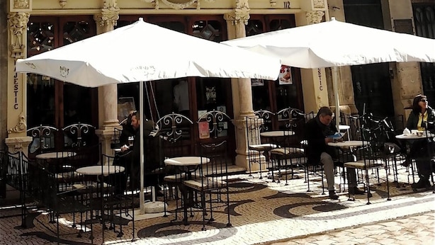 A cafe with outdoor seating, ornate architectural details, and a white awning.