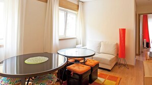 A modern living room with a round glass table, a white sofa, and a colorful rug.