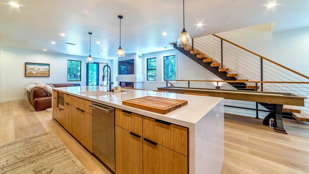 Une cuisine moderne avec des meubles en bois, un îlot central, des luminaires suspendus et un escalier menant à un niveau supérieur.