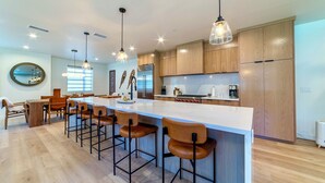 Une cuisine moderne dotée d’un grand îlot central, de tabourets de bar, de meubles en bois et de luminaires suspendus.