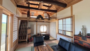 Una habitación tradicional japonesa con suelo de tatami, techo bajo con vigas de madera a la vista, una mesa de tatami, un sofá de cuero negro y puertas correderas shoji.