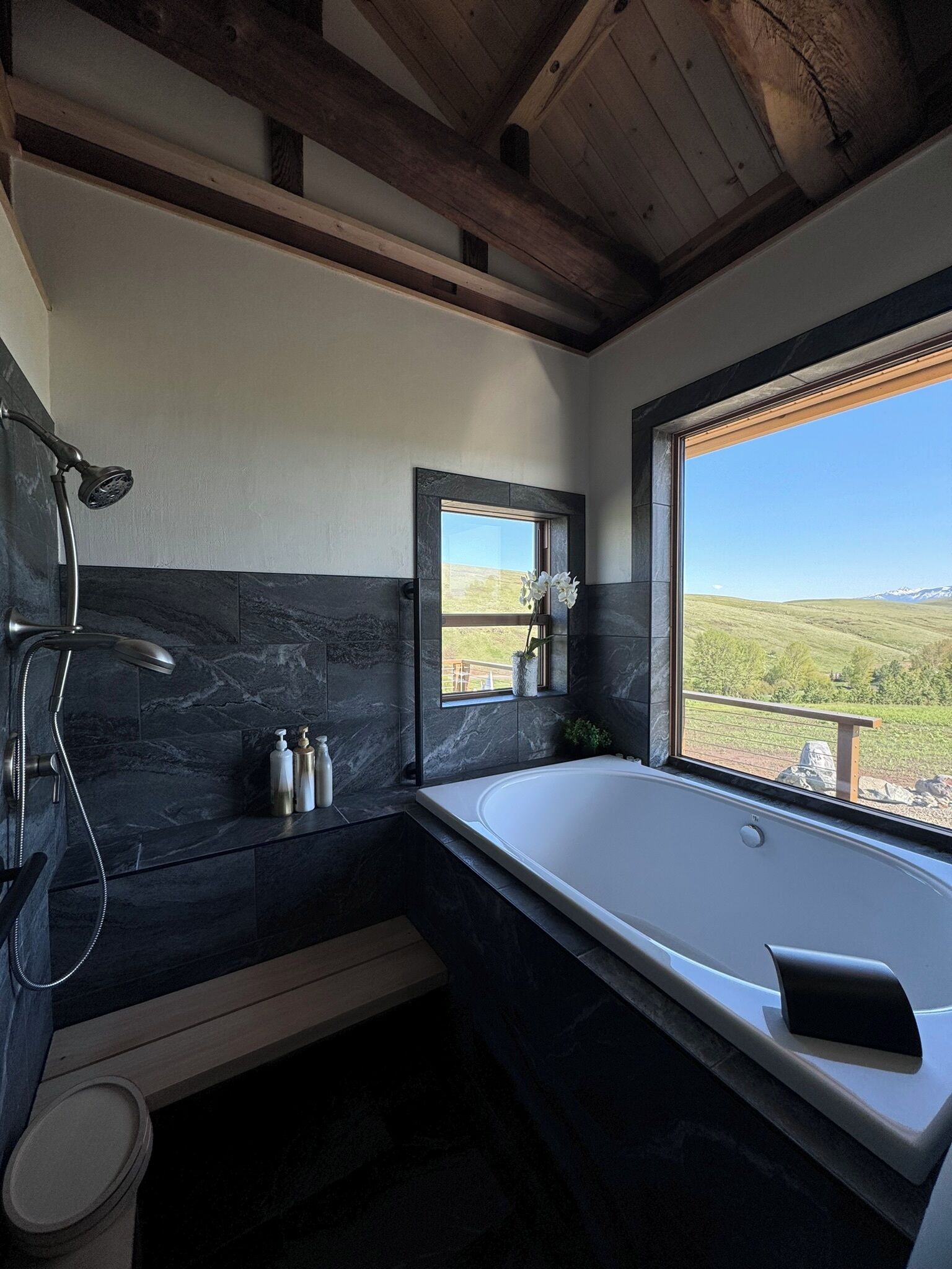 A modern bathroom with a large bathtub, a shower, and a window offering a view of the countryside.