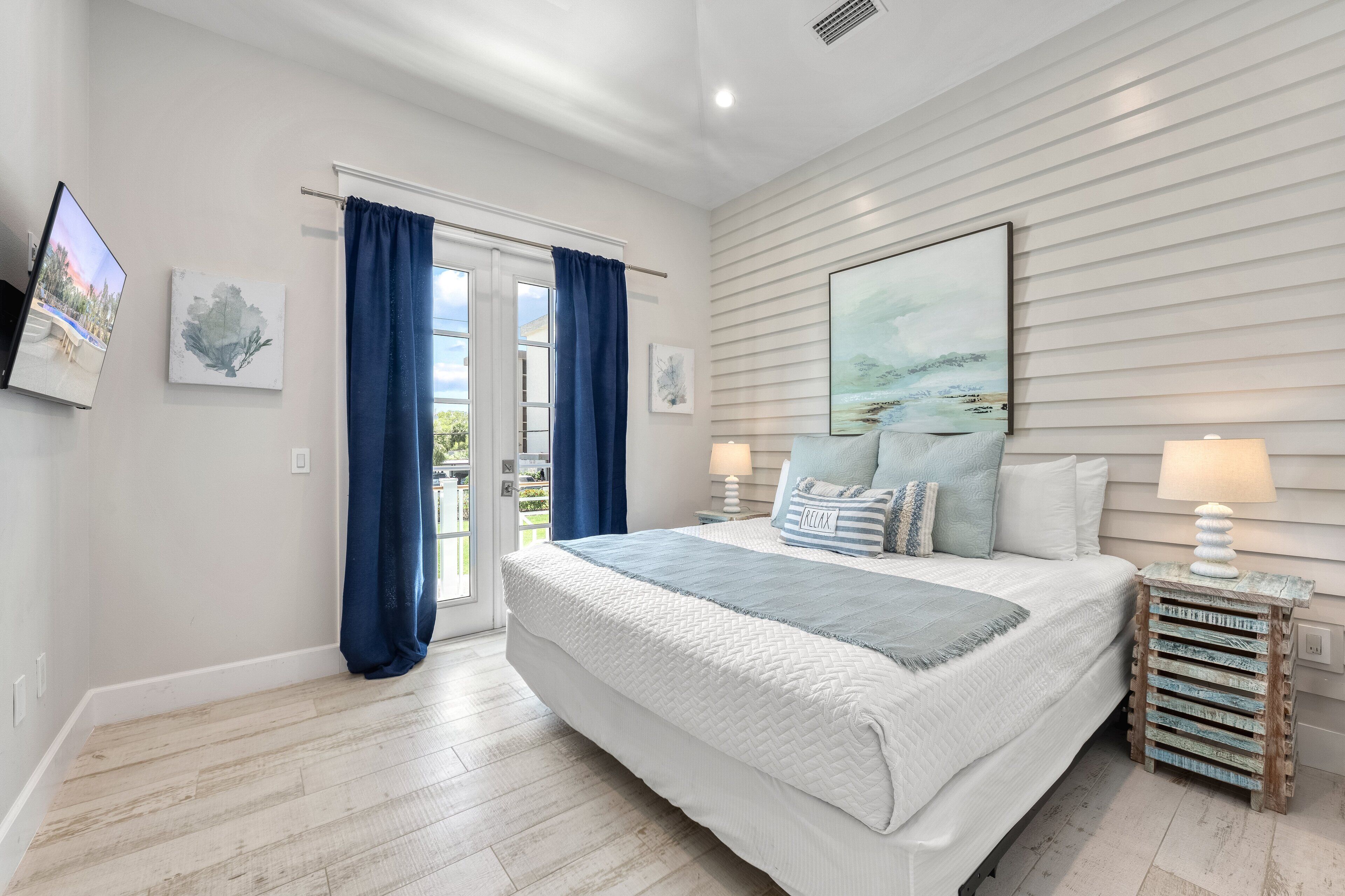 A bedroom with a large bed, a view through a glass door, and a painting on the wall.