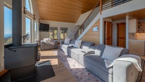 Un soggiorno moderno con un ampio divano modulare grigio, soffitto in legno e una scala che conduce a un livello superiore.