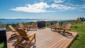 Una terrazza con sedie di legno e un barbecue, con vista su un paesaggio montuoso e un lago.