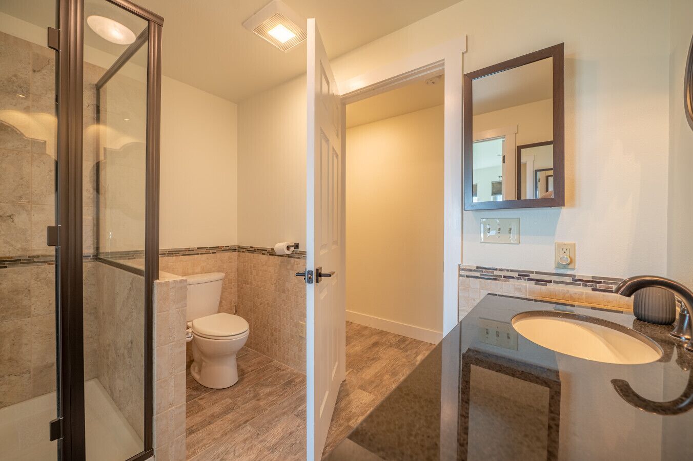 A bathroom with a glass shower enclosure, a toilet, a sink with a mirror, and a tiled floor.